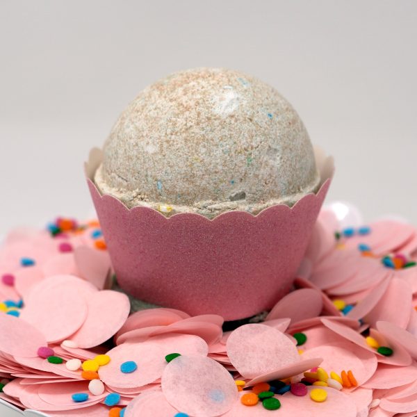 Colorful CBD bath bomb in pink cupcake wrapper on top of pile of pink and rainbow confetti
