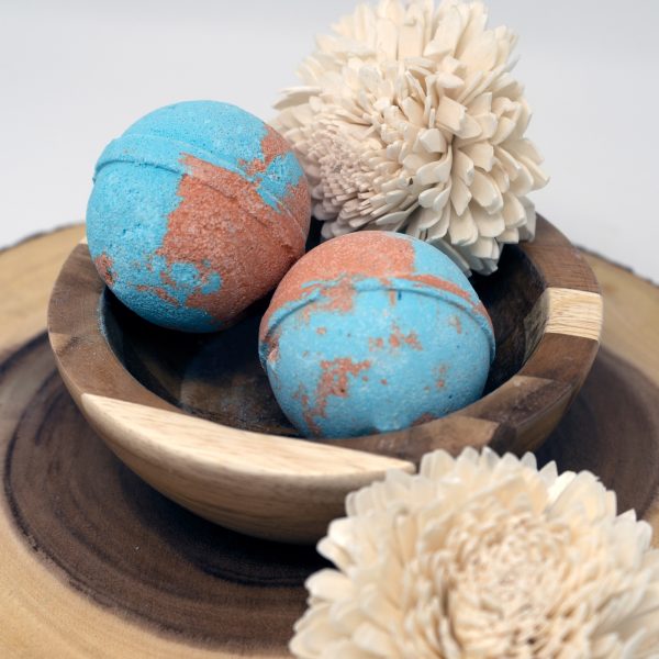 2 blue and orange sandalwood bath bombs in a wooden bowl with white flowers.