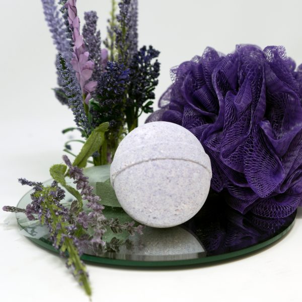 Light purple cbd bath bomb on small round mirror with purple loofah and lavender flowers