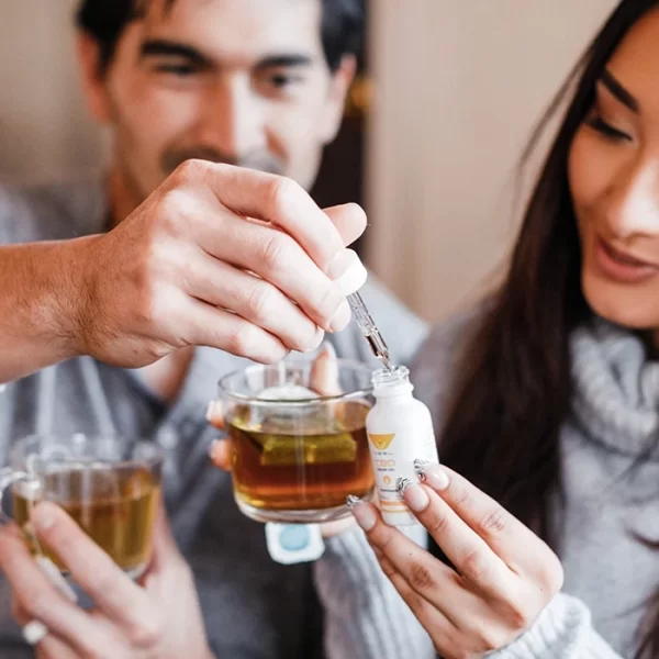 Man and woman holding glass cups of tea take a full dropper from unflavored broad spectrum hemp oil tincture
