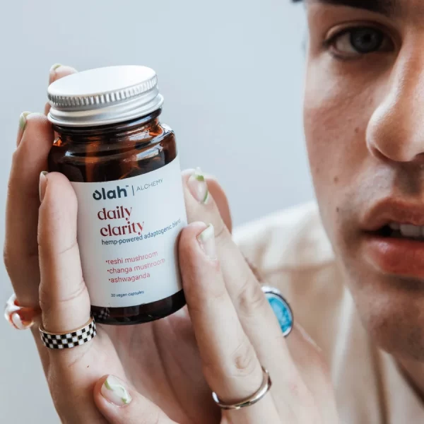 Person holds a bottle of olah brand alchemy daily clarity hemp-powered capsules close to their face